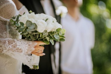 Valmiera, Letonya - 15 Ağustos 2024 - Açık hava seremonisi sırasında elinde dantel bir elbise, elinde bir buket gül tutan bir gelinin yakın çekimi.