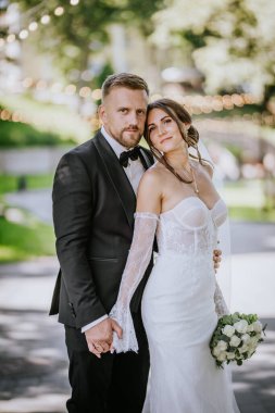 Valmiera, Letonya - 15 Ağustos 2024 Gelin ve damat, gelin ile el ele tutuşup, başını damatların omuzlarına yaslayarak, sakin ve aşık bir şekilde poz veriyorlar.