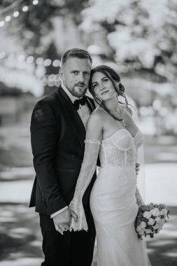 Valmiera, Letonya - 15 Ağustos 2024 - Gelin ve damat el ele tutuşmuş, gelinin başını damatların omuzlarına dayamış, romantik bir anda kameraya bakıyor.