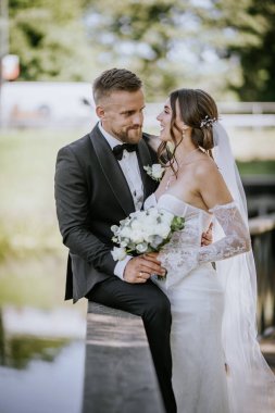 Valmiera, Letonya - 15 Ağustos 2024 - Bir gelin ve damat açık havada neşeli bir anı paylaşıyor. Gelin bir buket beyaz gül tutarken damat ona gülümsüyor..