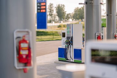 Valmiera, Letonya - 8 Ağustos 2024 - Benzin pompaları ve yangın söndürücüleri sütunlara monte edilmiş modern bir benzin istasyonu, güneşli bir günde arka planda açık fiyatlandırmanın yer aldığı.