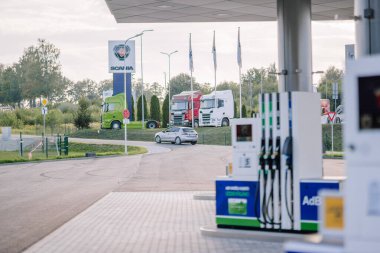 Valmiera, Letonya - 8 Ağustos 2024 - Önünde benzin pompaları olan bir benzin istasyonu, açık bir günde arka planda park halindeki kamyonları olan bir İskandinav bayii görülüyor.