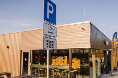 Valmiera, Letonya - 8 Ağustos 2024 - Güneşli bir günde ahşap kaplamalı ve büyük pencereli modern bir binanın yakınına park yeri tabelası.