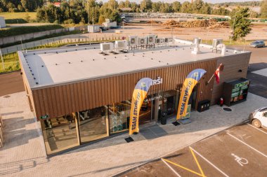 Valmiera, Letonya - 8 Ağustos 2024 - Çatıda bayrakları, park alanları ve görünür klimaları olan modern bir Virsi marketinin havadan görünüşü.