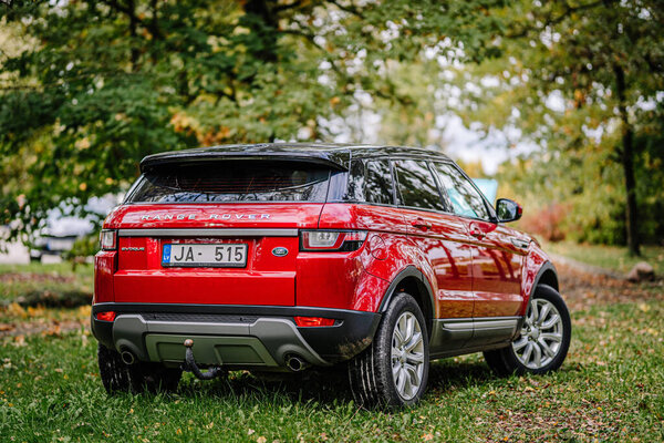 Valmiera, Latvia - October 4, 2024 - A red Range Rover Evoque parked on grass with a forest background, showcasing the rear view and license number.