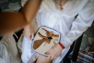 Valmiera, Latvia - August 24, 2024 - Reflection of a makeup artist applying makeup on a woman, captured in a handheld mirror. The setting is intimate and focused on the beauty routine. clipart