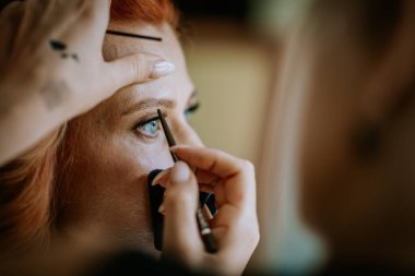 Valmiera, Letonya - 24 Ağustos 2024 - Güzellik başvuru sürecinde hassasiyet ve detaylara odaklanmış bir kadın gözüne göz kalemi süren bir makyaj sanatçısının yakın çekimi