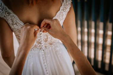 Valmiera, Latvia - August 24, 2024 - Close-up of a womans hands fastening buttons on a lace wedding dress, capturing a delicate and intimate moment before the ceremony clipart