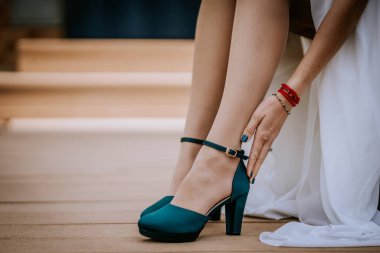 Valmiera, Letonya - 24 Ağustos 2024 - Yüksek topuklu ayakkabılarını ahşap bir güvertede düzelten bir kadının yakın çekimi, ayak bileği kayışı ve ellerinin ve aksesuarlarının hassas ayrıntıları üzerine odaklanıyor..