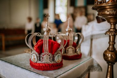 Valmiera, Letonya - 24 Ağustos 2024 - Kırmızı kadife ve dini simgelerle süslenmiş iki gümüş taç, bir kilise ortamında bir masaya yerleştirilmiş, bir düğün veya dini tören için hazırlanmıştır..