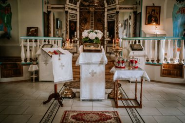 Valmiera, Letonya - 24 Ağustos 2024 - Bir tören için hazırlanmış taç, mum ve dini simgelerle süslü kilise sunağı. İç kısmı beyaz çarşaflar ve altın aksanlarla süslenmiş..