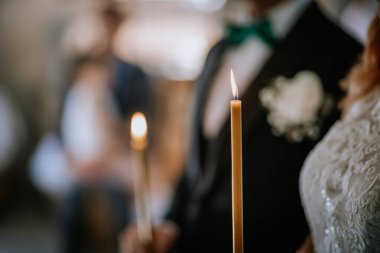 Valmiera, Letonya - 24 Ağustos 2024 - Düğün töreninde tutulan mum alevinin yakın çekimi, arka plandaki çifte odaklanarak, sakin ve samimi bir atmosfer yaratıyor..