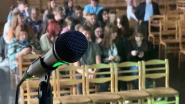 Arka planda bulanık bir dinleyici kitlesi olan bir mikrofonun yakın plan görüntüsü, 4K 'deki canlı performans veya konuşmadan bir dakika öncesini kaydediyor..