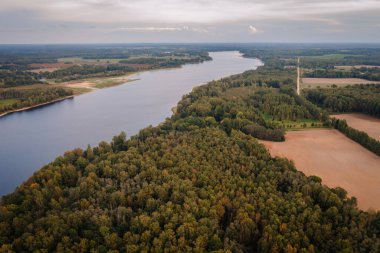 Yoğun ormanlar, tarlalar ve bulutlu bir günde dolambaçlı toprak bir yol olan nehir manzarası huzurlu bir doğal manzara sunuyor..