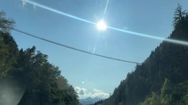 Tirol, Avusturya - 15 Eylül 2024 - 179 no 'lu asma köprü, güneşli bir gökyüzünün altındaki iki ormanlık dağ zirvesi boyunca uzanır ve mavi gökyüzü ile çarpıcı bir zıtlık yaratır..