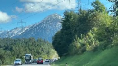 Tirol, Avusturya - 15 Eylül 2024 Karla kaplı dağ, elektrik hatları, ağaçlar ve arabalarla berrak mavi gökyüzü altında manzaralı bir yolda.