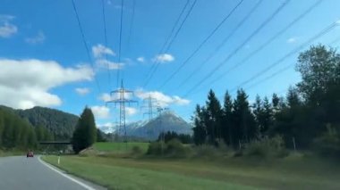 Tirol, Avusturya - 15 Eylül 2024 Bir dağ manzarası boyunca uzanan elektrik hatları, arka planda karla kaplı zirveler ve açık mavi gökyüzü.