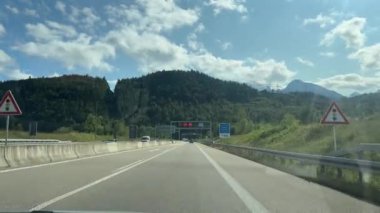Tirol, Avusturya - 15 Eylül 2024 - Güneşli bir günde Avusturya Cumhuriyeti tabelası, dağ manzarası ve dijital hız limitleri olan bir araba bir sınır tüneline yaklaşıyor.