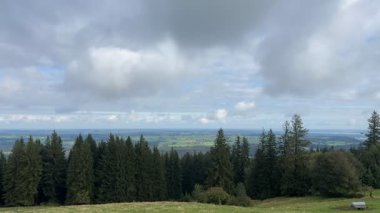 Yoğun çam ormanı, açık alanlar ve bulutlu bir gökyüzü ile geniş bir arazinin zamanı, dingin bir vadi üzerindeki değişen hava modellerini yakalıyor..