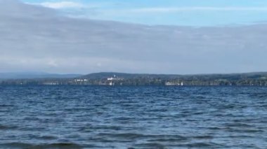 Bavyera, Almanya - 15 Eylül 2024 - Uzak kıyı şeridi ve ormanlık tepeleri olan sakin bir göl.