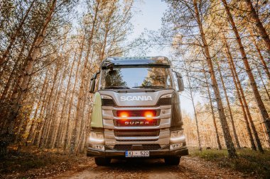 Gulbene, Latvia - October 15, 2024 - A Scania truck with a visible SUPER logo, front view, is parked on a forest road surrounded by tall trees with autumn colors clipart