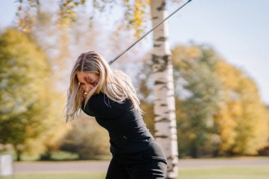 Yüzünde sahte pençe izleri olan bir kadın güneşli bir günde arka planda sonbahar ağaçlarıyla dışarıda golf salıncağını bitiriyor..