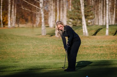 Golf sahasında yüzünde sahte pençe izleri olan bir kadın elinde golf sopasıyla atış yapmaya hazırlanıyor..