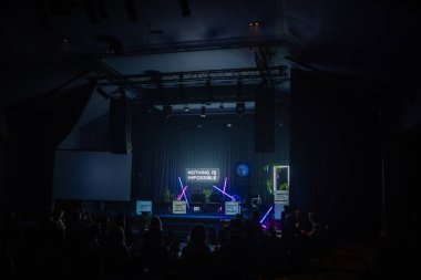 Valmiera, Letonya - 18 Ekim 2024 - yapay zeka konferansı. Karanlık bir konferans sahnesi, neon lambaları ve hiçliği olan imkansız bir işaret, ön planda seyirci siluetleri var.