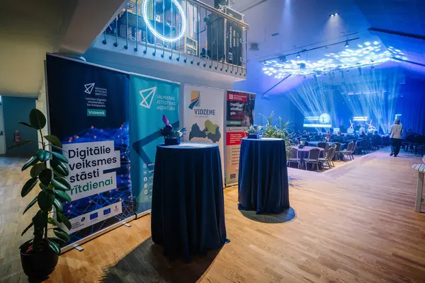 Valmiera, Letonya - 18 Ekim 2024 - yapay zeka konferansı. Sancaklar, yüksek tablolar, bitkiler ve arka planda sahne aydınlatma ve dijital görüntülerin yer aldığı bir konferans salonu ile modern bir etkinlik düzenlenmiştir..