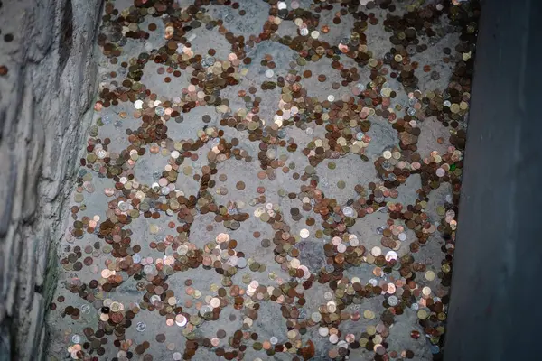 Vilnius, Lithaunia - 22 Ekim 2024 - Taştan bir yüzeye saçılmış sayısız madeni paranın yakın görüntüsü, adak veya dilekleri simgeliyor..