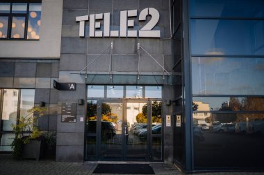 Riga, Letonya - 25 Ekim 2024 - Kapısında Tele2 logosu olan ve pencerelerinde yansımaları olan modern bir binanın girişi