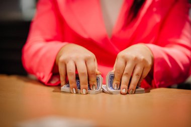 Riga, Latvia - October 25, 2024 - A person in a bright pink outfit shuffling playing cards on a wooden table, with close focus on their hands and metallic nail polish. clipart