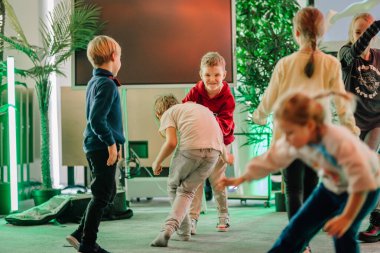 Riga, Letonya - 25 Ekim 2024 - Peter Pan Partisi etkinliği sırasında çocuklar ev ortamında yeşil ve renkli ışıklarla çevrili bir şekilde gülüp oynuyorlar..