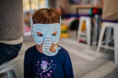 Riga, Latvia - October 25, 2024 - A child wearing a handmade blue elephant mask during the Peter Pan Party, standing indoors with a focused expression. clipart