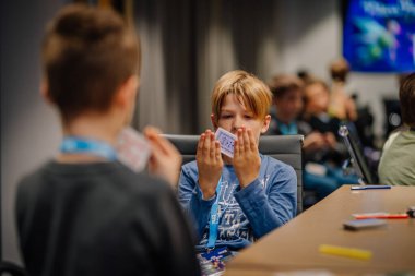 Riga, Letonya - 25 Ekim 2024 - Peter Pan Partisi etkinliği sırasında masada kağıt oynayan iki çocuk, biri elindeki kartlara odaklanmış..