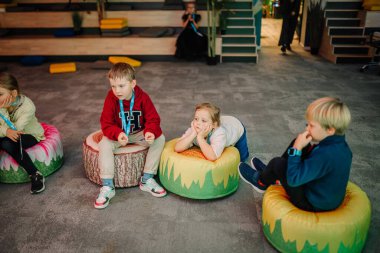 Riga, Letonya - 25 Ekim 2024 - Çocuklar Peter Pan Partisi sırasında temalı yastıklarda oturur, düşünceli ve rahat görünürler..