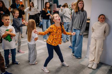 Riga, Letonya - 25 Ekim 2024 - Genç bir kız coşkuyla PETER PAN Parti 'sinde oyun oynuyor, diğer çocuklar tarafından çevrelenmiş, enerjik bir şekilde hareket ediyor ve neşeli ifadeler sergiliyor..