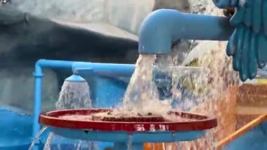 Vilnius, Lithaunia - 23 Ekim 2024 - Su parkı ortamında mavi borulardan kırmızı bir havuza akan yakın çekim. Çocuklar için etkileşimli ve renkli elementler.