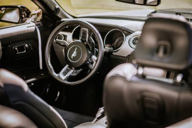 Valmiera, Letonya - 24 Ağustos 2024 - Mustang logosu, gösterge paneli ve siyah deri koltukları olan direksiyon simidine odaklı modern bir arabanın iç görünümü.