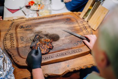 Valmiera, Latvia - November 7, 2024 - A grilled steak on a wooden cutting board engraved with Latvijas Steiku Klubs, with a gloved hand holding a knife ready to slice