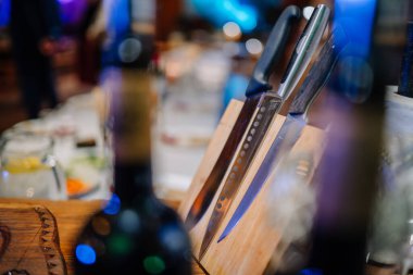 A set of kitchen knives with various blades is displayed in a wooden knife block on a table, surrounded by blurred background elements and lights. clipart