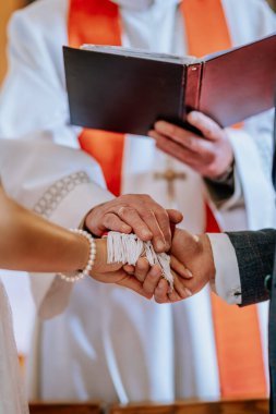 Koknese, Latvia - September 26, 2023 - A priest performs a wedding hand-fasting ceremony, wrapping the couples hands together with a symbolic white cord as a gesture of unity and blessing clipart