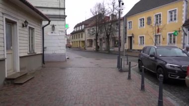 Cesis, Letonya - 13 Kasım 2024 - Eski bir kasabada sakin bir kaldırım taşı caddesi tarihi binalar, atölye işaretleri ve bulutlu bir günde park edilmiş bir araba, huzurlu bir şehir manzarası.