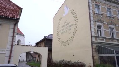 Cesis, Letonya - 13 Kasım 2024 - Bulutlu bir günde, eski bir kasabada, kemer ve tarihi bir mimarinin yakınındaki bir bina duvarına güvercin ve barış mesajı içeren bir duvar resmi.