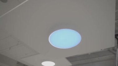 Yumuşak mavi bir parıltıyla modern tavan lambasına yakın çekim yapmak odada sakinleştirici ve fütüristik bir ortam yaratıyor..