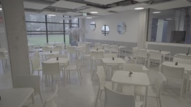 Cesis, Letonya - 13 Kasım 2024 - Beyaz masalı, sandalyeli, minimalist dekorlu ve geniş pencereli modern kafe iç mimarisi.