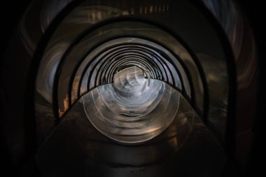 Parnu, Estonia - July, 25, 2024 - A view down a dark, twisting tubular slide tunnel with light reflections, creating a mesmerizing spiral effect as it narrows in the distance. clipart