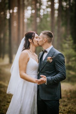 Koknese, Letonya - 26 Eylül 2023 Gelin ve damat, barışçıl ve doğal bir atmosferde aşklarını kutlarken bir orman ortamında şefkatli bir öpücük paylaşıyorlar..