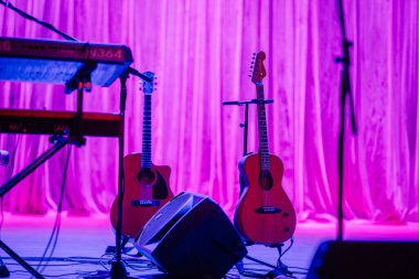 Aloja, Letonya - 16 Kasım 2024 - Akustik gitarlar, bir klavye ve mor perde arkaplanı olan sahnede bir hoparlör, canlı performans veya konser için hazırlar..