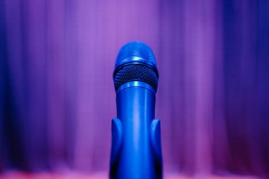 Close-up of a microphone in a stand with a vibrant purple-lit background. Perfect for themes of music, performance, or public speaking. clipart